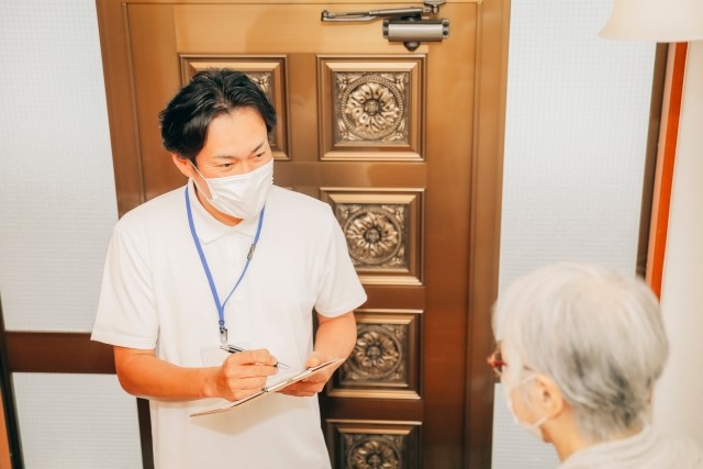 玄関で高齢者の女性と話しながらメモをを取る男性