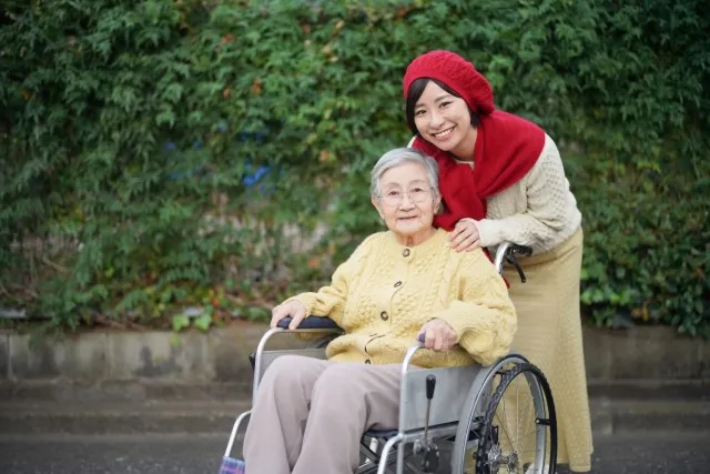 福祉用具の車椅子に乗る高齢者女性とそれを押す赤い頭巾をかぶった女性