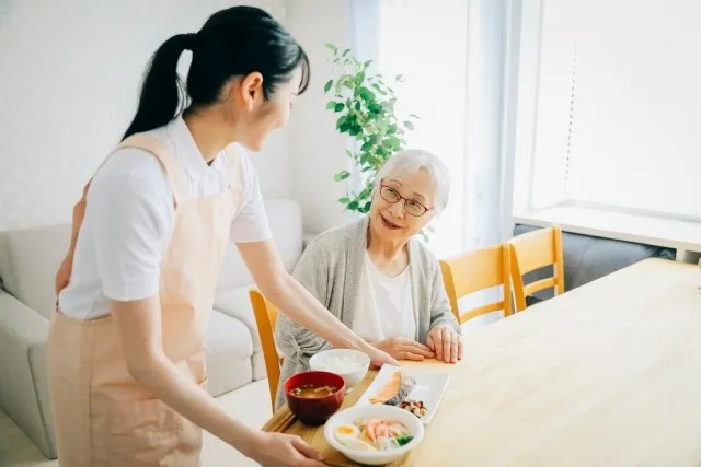 高齢者の女性に介護食を配膳する若い女性介護士